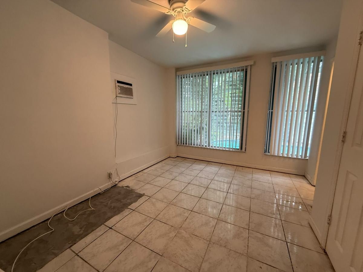 Bedroom with dated tile flooring and plain white walls before renovation