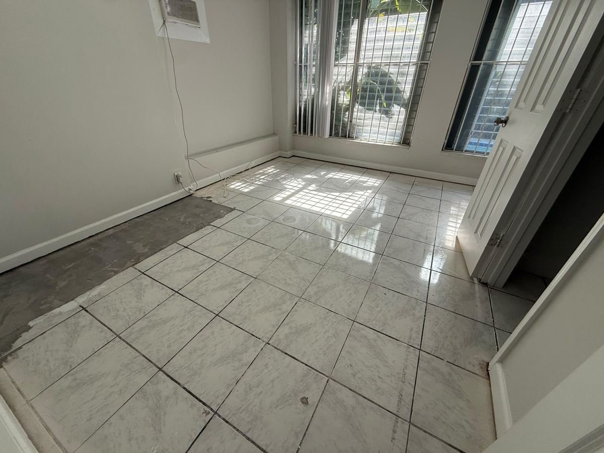 Room with worn tile flooring and patched subfloor before renovation